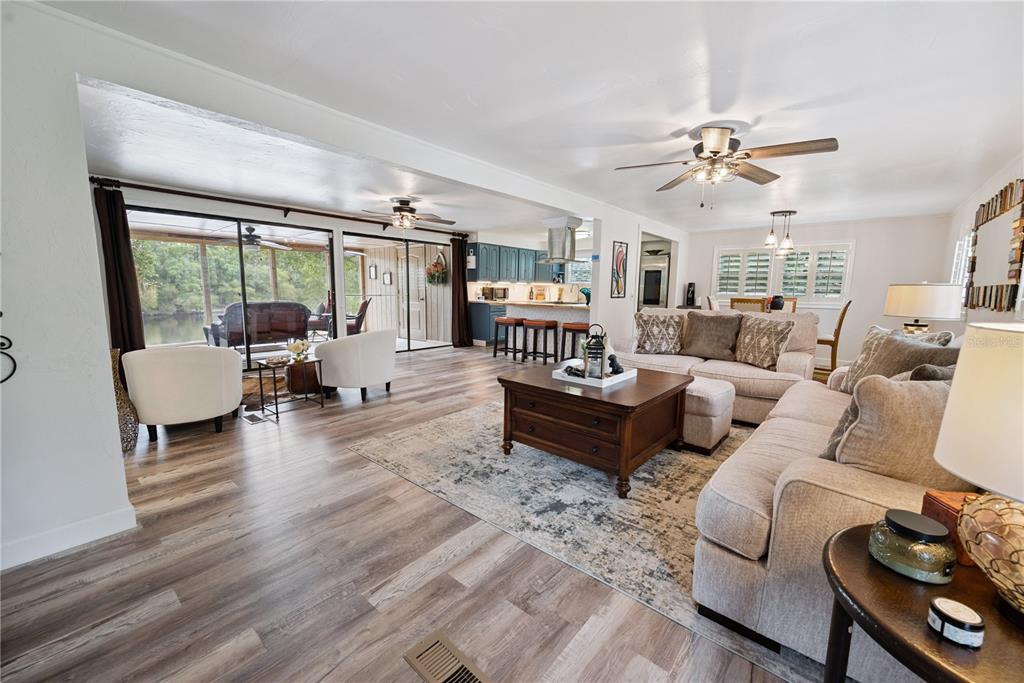 An open-concept living room features wood-look flooring, a kitchen with blue cabinets, and a screened porch — 102 NE 931ST STREET, BRANFORD, FL