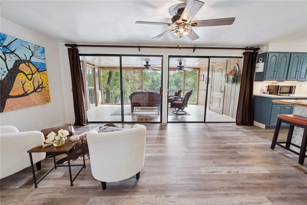 A living room with wood-look flooring, white armchairs, and sliding glass doors opening to a porch — 102 NE 931ST STREET, BRANFORD, FL