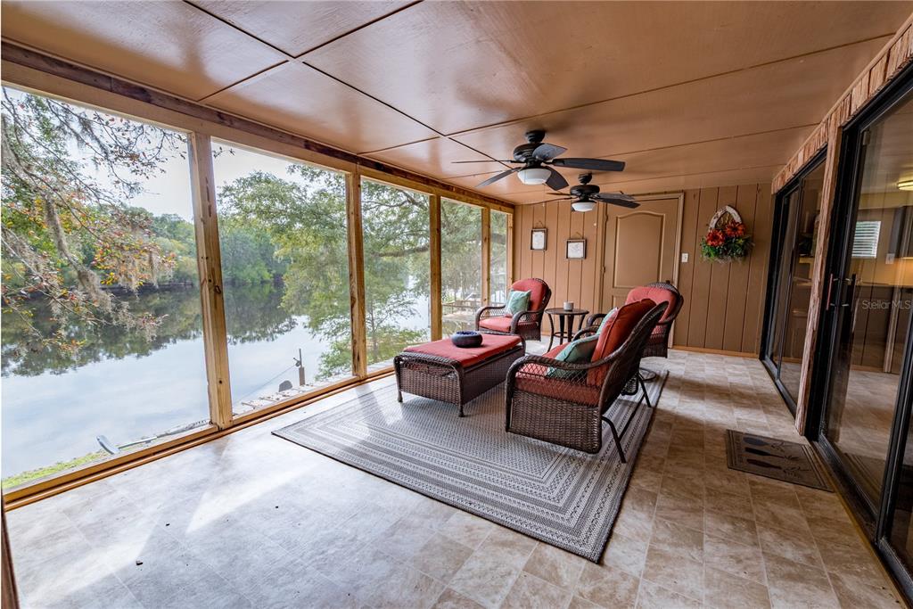 A screened-in porch with tile flooring, wicker furniture, and a view of a river — 102 NE 931ST STREET, BRANFORD, FL