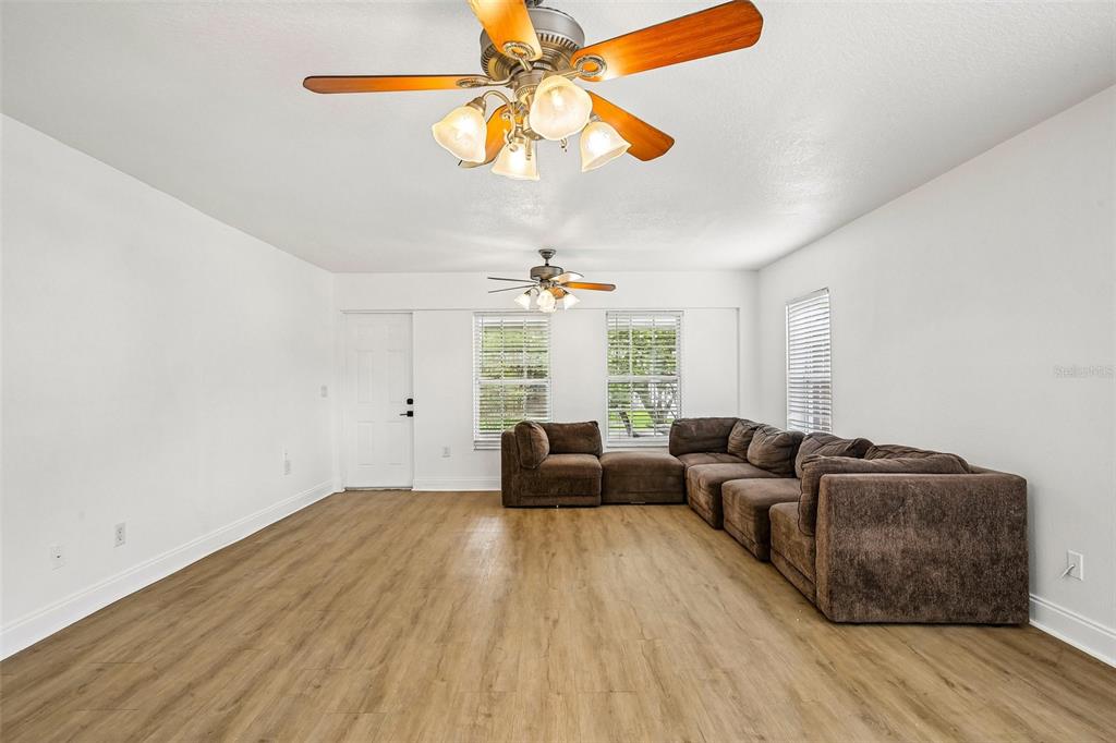 A living room features light wood-look flooring, white walls, two ceiling fans, and a brown sectional — 1539 VALENCIA STREET, CLEARWATER, FL
