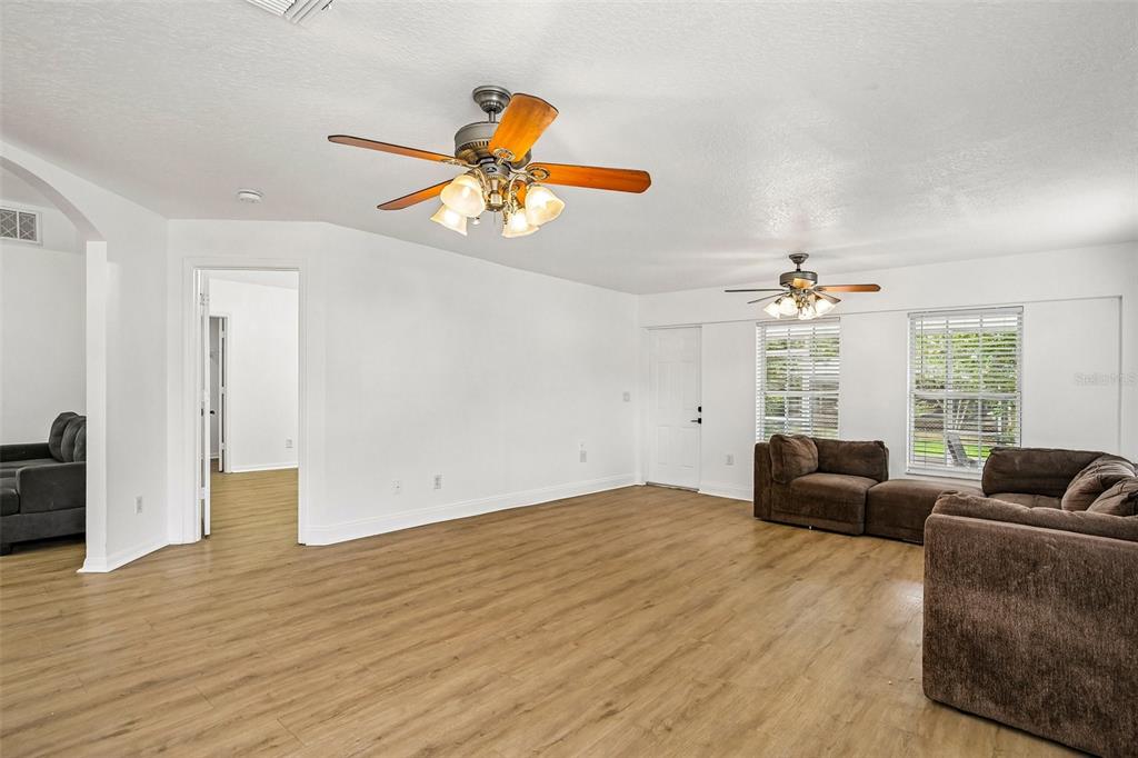 A spacious living room features light wood-look flooring, white walls, and two ceiling fans — 1539 VALENCIA STREET, CLEARWATER, FL