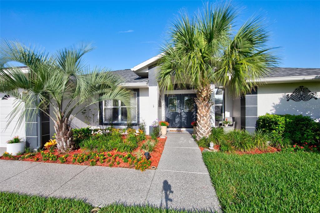 A single-story house exterior features a concrete walkway leading to double front doors and palm trees — 11117 TWOSOME DRIVE, SAN ANTONIO, FL