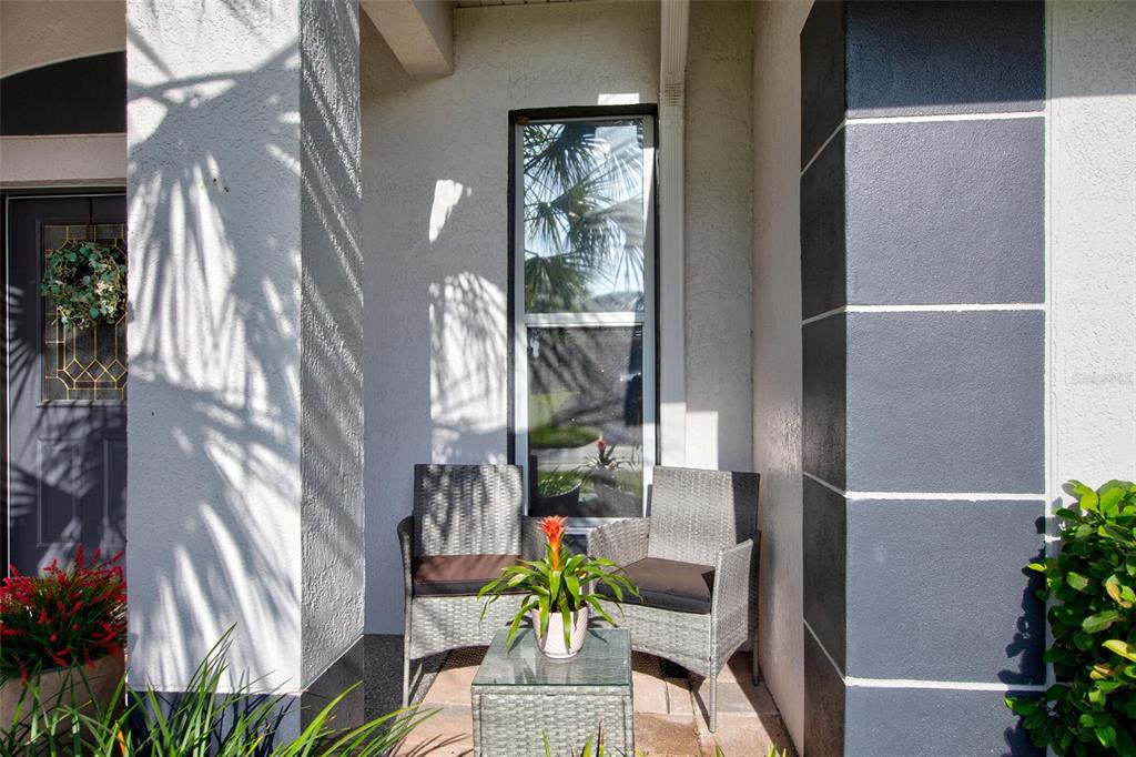 A small covered porch features two wicker chairs, a glass side table, and a potted plant — 11117 TWOSOME DRIVE, SAN ANTONIO, FL