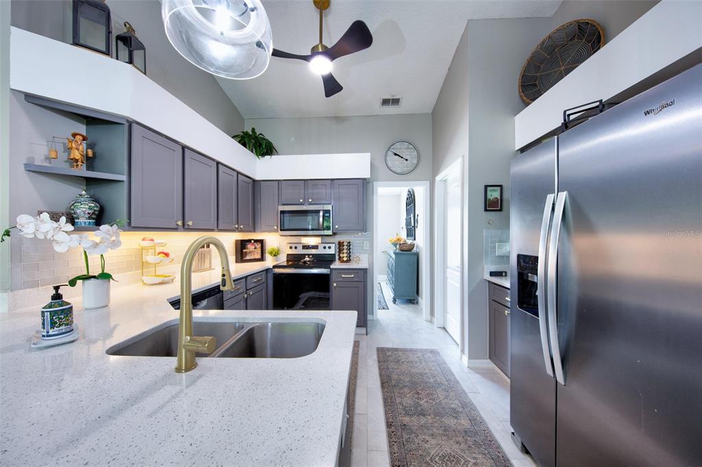 A kitchen features gray cabinets, white quartz countertops, stainless steel appliances, and a gold faucet — 11117 TWOSOME DRIVE, SAN ANTONIO, FL