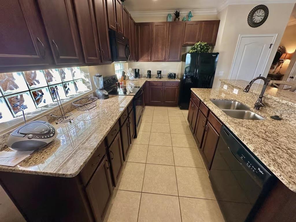 A kitchen with dark wood cabinets, granite countertops, tile flooring, and black appliances — 4353 ACORN COURT, DAVENPORT, FL