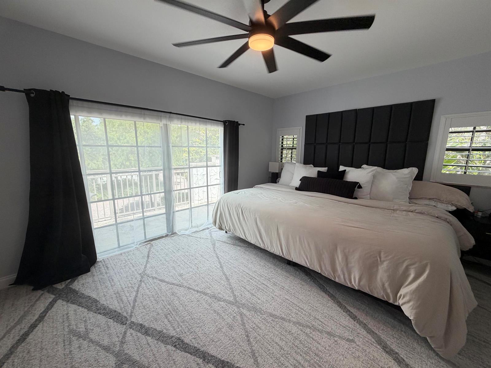 A bedroom features a large bed with a black headboard, ceiling fan, and sliding glass doors — 4400 Hidden Harbour Terrace, Dania Beach FL 33312, DANIA BEACH, FL