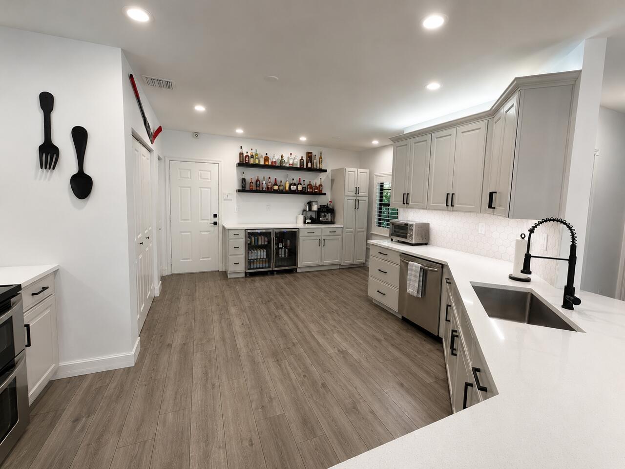 A modern kitchen features light gray cabinets, white countertops, a beverage fridge, and wood-look flooring — 4400 Hidden Harbour Terrace, Dania Beach FL 33312, DANIA BEACH, FL