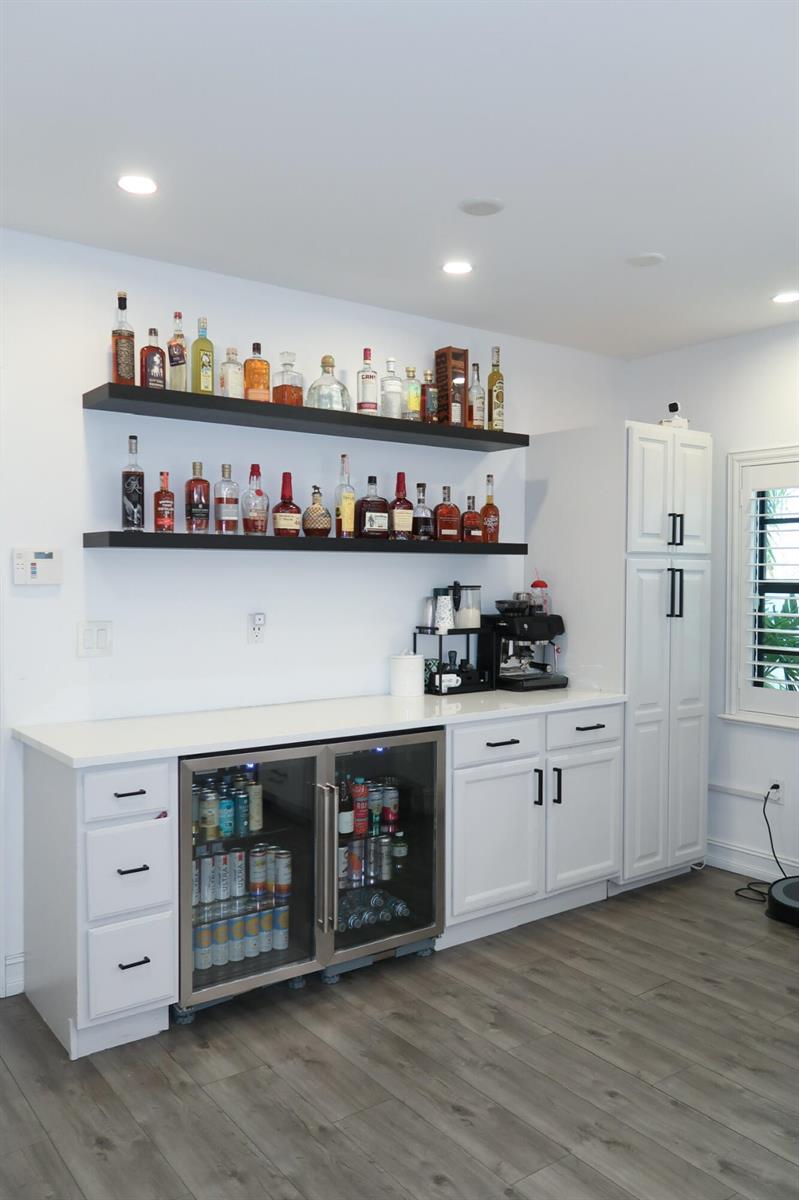A home bar area features white cabinets, a beverage refrigerator, and two black floating shelves — 4400 Hidden Harbour Terrace, Dania Beach FL 33312, DANIA BEACH, FL