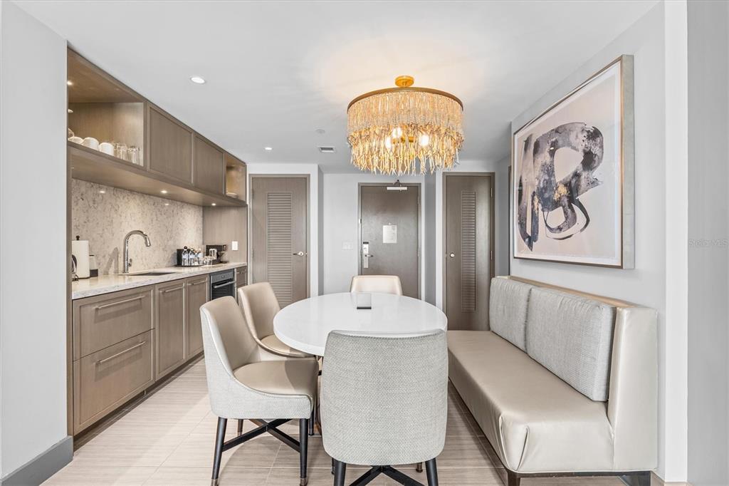 A dining area features a white oval table, upholstered chairs, a bench, and a kitchenette — 691 S GULFVIEW BOULEVARD UNIT 815, CLEARWATER BEACH, FL