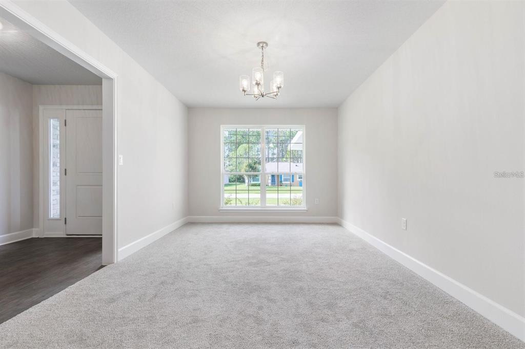 A carpeted dining room with a central chandelier and a large window overlooking the yard — 34 RYMSHAW DRIVE, PALM COAST, FL