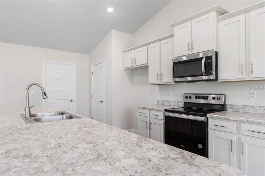 A kitchen features white cabinets, granite countertops, a stainless steel microwave, and a kitchen island — 34 RYMSHAW DRIVE, PALM COAST, FL