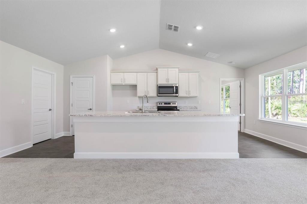 A kitchen with white cabinets, a granite-topped island, and stainless steel appliances under a vaulted ceiling — 34 RYMSHAW DRIVE, PALM COAST, FL