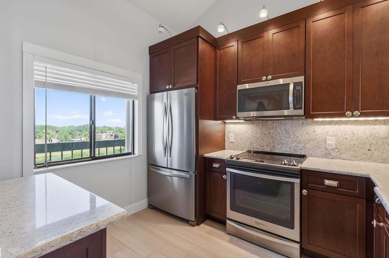 A kitchen features dark wood cabinets, stainless steel appliances, granite countertops, and a window view — 701 Seafarer Circle # 504, Jupiter FL 33477, JUPITER, FL