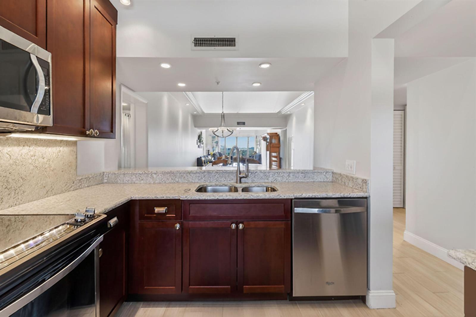 A kitchen with dark wood cabinets, granite countertops, and stainless steel appliances overlooks a living area — 701 Seafarer Circle # 504, Jupiter FL 33477, JUPITER, FL