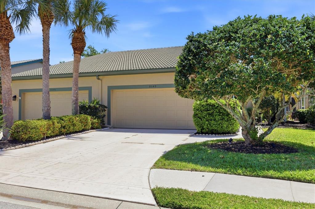 A beige house exterior features a two-car garage, a concrete driveway, and palm trees — 8549 54TH AVENUE CIRCLE E, BRADENTON, FL