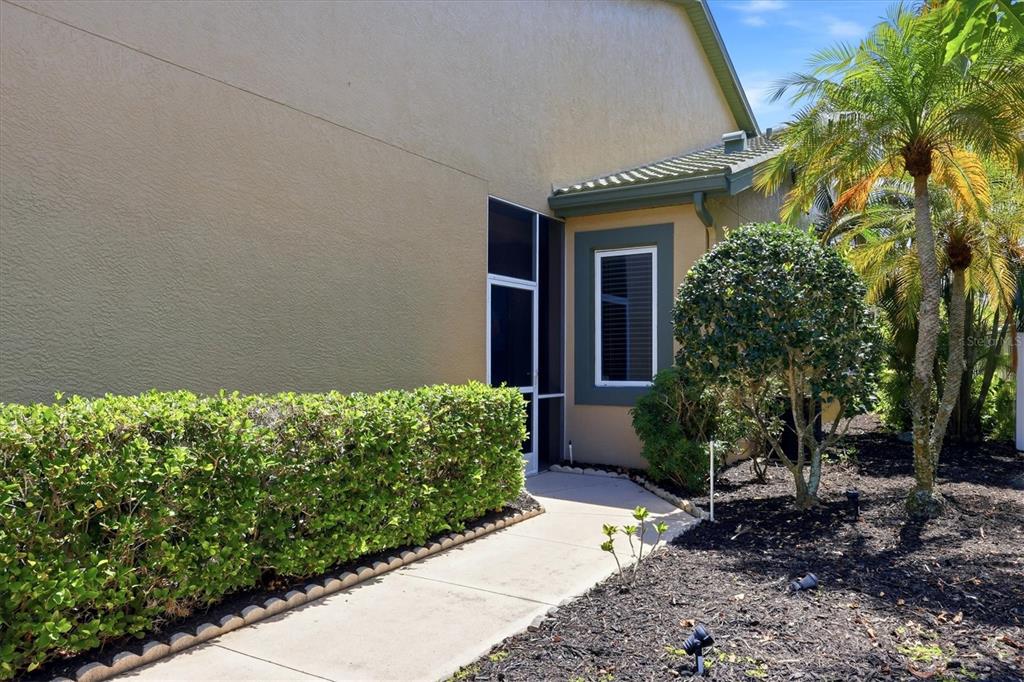 A concrete walkway leads to a screened entryway beside a beige house with landscaping — 8549 54TH AVENUE CIRCLE E, BRADENTON, FL