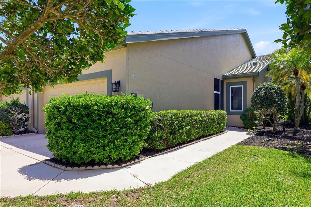 A beige house exterior features a concrete walkway, a manicured hedge, and a garage — 8549 54TH AVENUE CIRCLE E, BRADENTON, FL