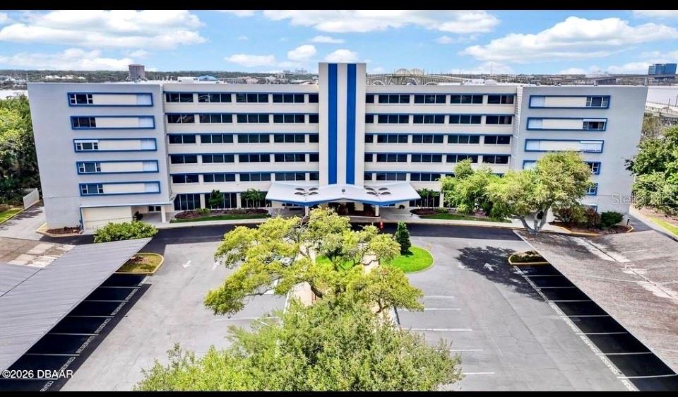 An aerial view of a multi-story apartment building with a parking lot and covered spaces — 1224 S PENINSULA UNIT 304, DAYTONA BEACH, FL