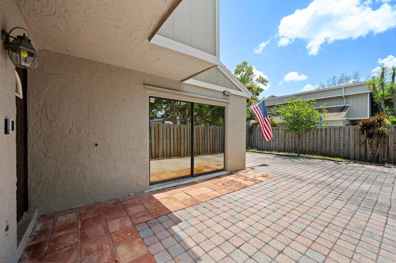 A patio with red tile and pavers features a sliding glass door and American flag — 620 Commodore Drive, Plantation FL 33325, PLANTATION, FL