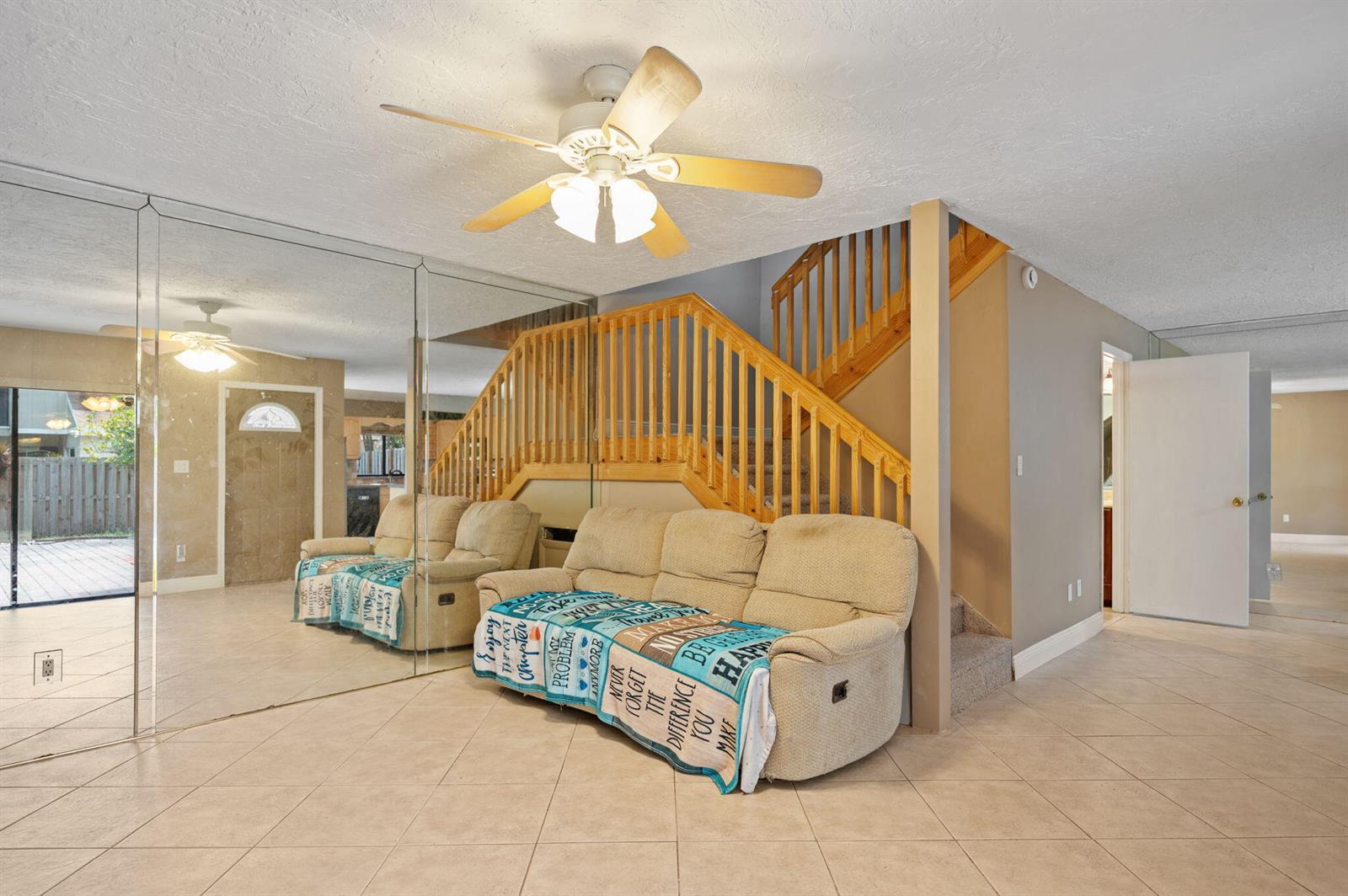 A living room features a beige reclining sofa, a mirrored wall, and a wooden staircase — 620 Commodore Drive, Plantation FL 33325, PLANTATION, FL