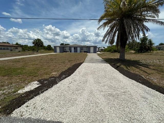 A gravel driveway leads to a single-story duplex under a bright, cloudy sky — 27285 SUNNYBROOK ROAD, PUNTA GORDA, FL