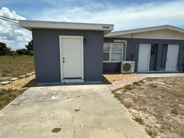 The exterior of a gray building features a concrete driveway, white doors, and an air conditioner — 27285 SUNNYBROOK ROAD, PUNTA GORDA, FL
