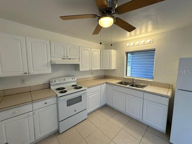A kitchen features white cabinets, tiled countertops, a white stove, and a ceiling fan — 27285 SUNNYBROOK ROAD, PUNTA GORDA, FL