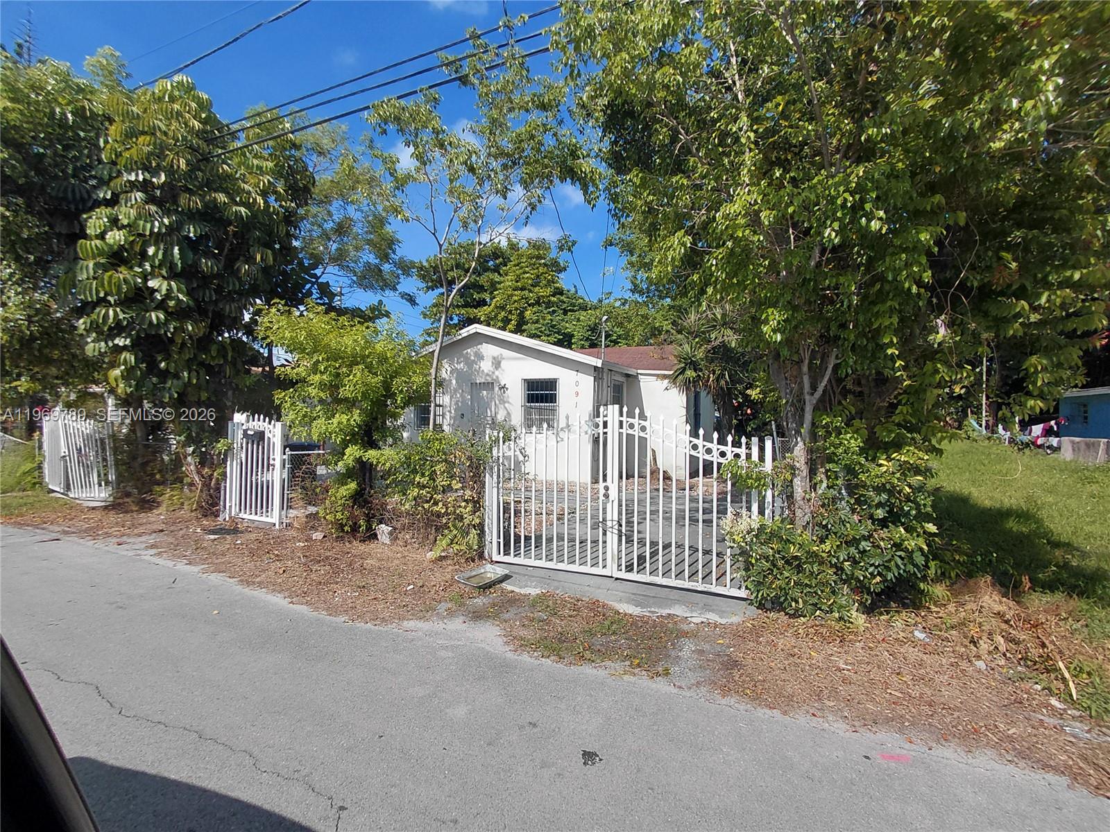A small, white, single-story house is enclosed by a white metal fence and gate — 7091 NW 21st Ave, Miami FL 33147, MIAMI, FL