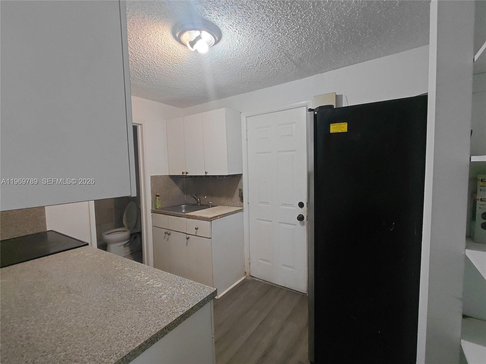 A small kitchen features white cabinets, a black refrigerator, and an adjacent bathroom — 7091 NW 21st Ave, Miami FL 33147, MIAMI, FL