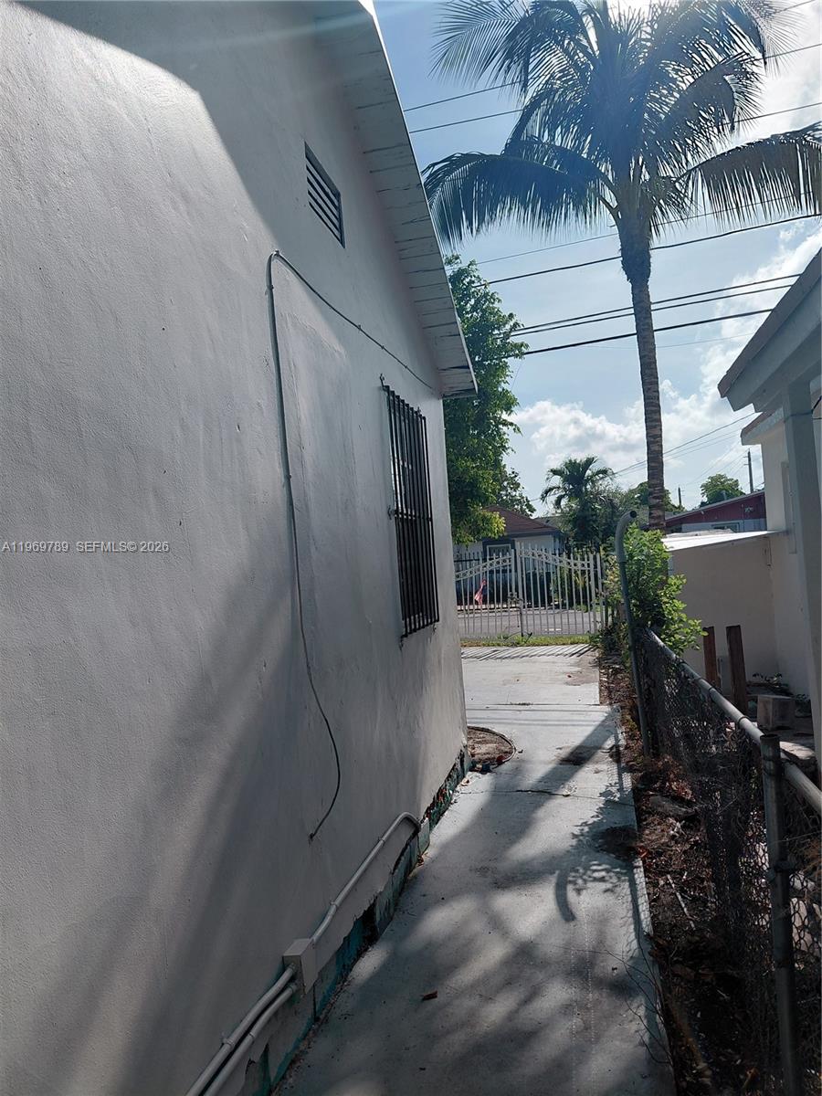 A narrow concrete walkway runs between a white exterior wall and a chain-link fence — 7091 NW 21st Ave, Miami FL 33147, MIAMI, FL