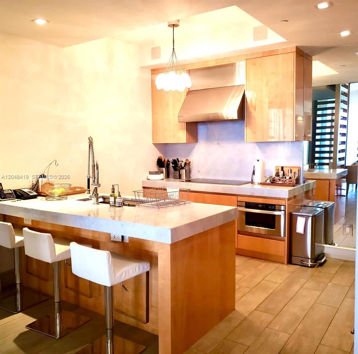 A modern kitchen features light wood cabinetry, a stone-topped island with bar seating, and stainless-steel appliances — 9705 Collins Ave # 2504N, Bal Harbour FL 33154, BAL HARBOUR, FL