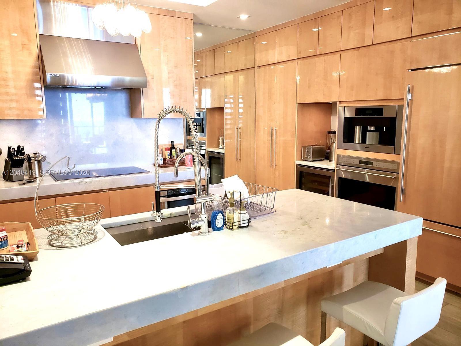 A modern kitchen features light wood cabinetry, a large stone island, and stainless steel appliances — 9705 Collins Ave # 2504N, Bal Harbour FL 33154, BAL HARBOUR, FL