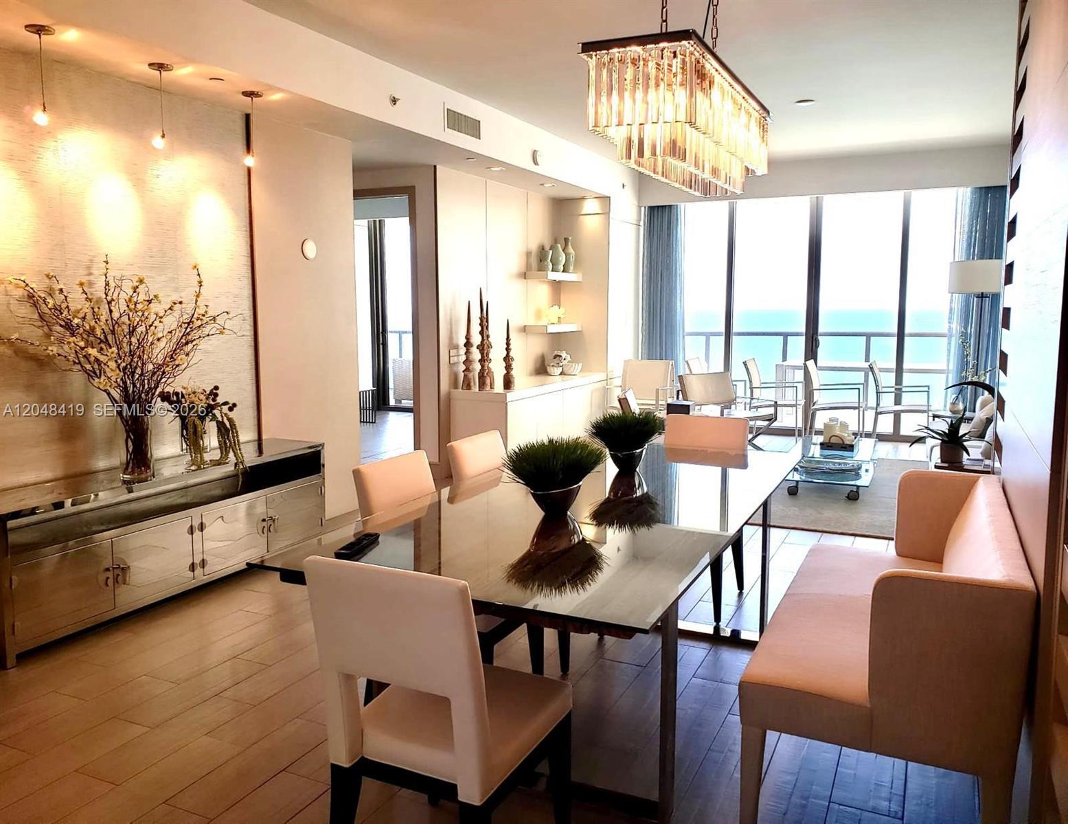 A dining room features a glass table, a light-colored bench, and a modern crystal chandelier — 9705 Collins Ave # 2504N, Bal Harbour FL 33154, BAL HARBOUR, FL