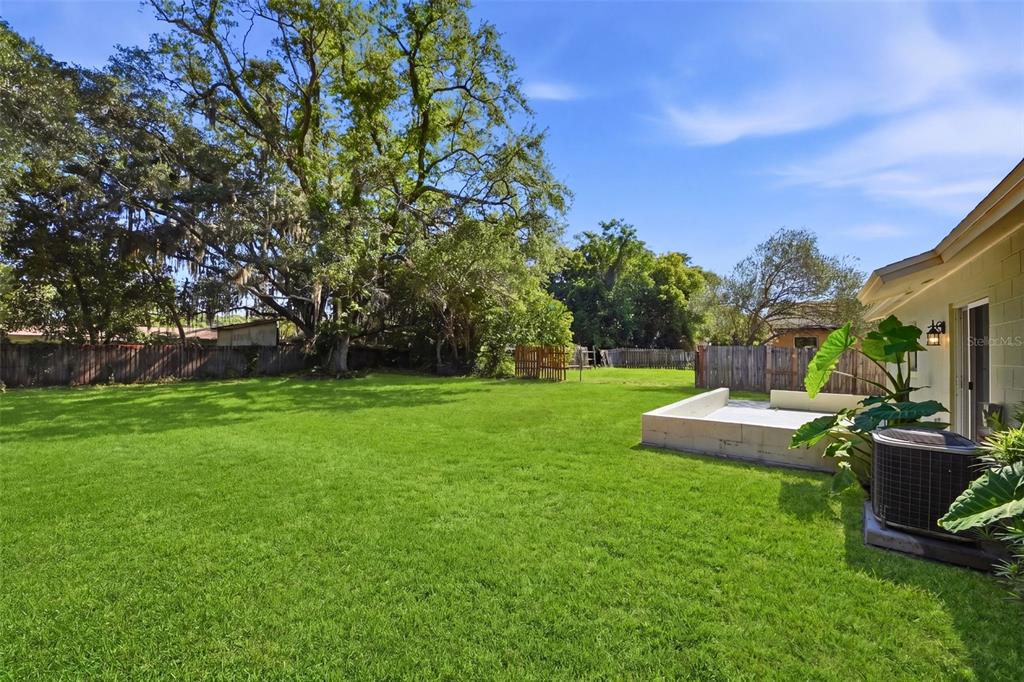 A grassy backyard features a large tree, a wooden fence, and a concrete patio area — 865 RICH DRIVE, OVIEDO, FL