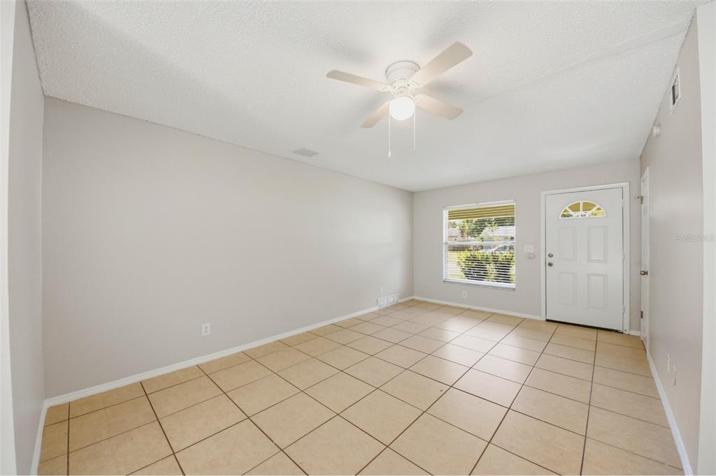 An empty room features light-colored walls, tan tile flooring, a ceiling fan, and a front door — 865 RICH DRIVE, OVIEDO, FL