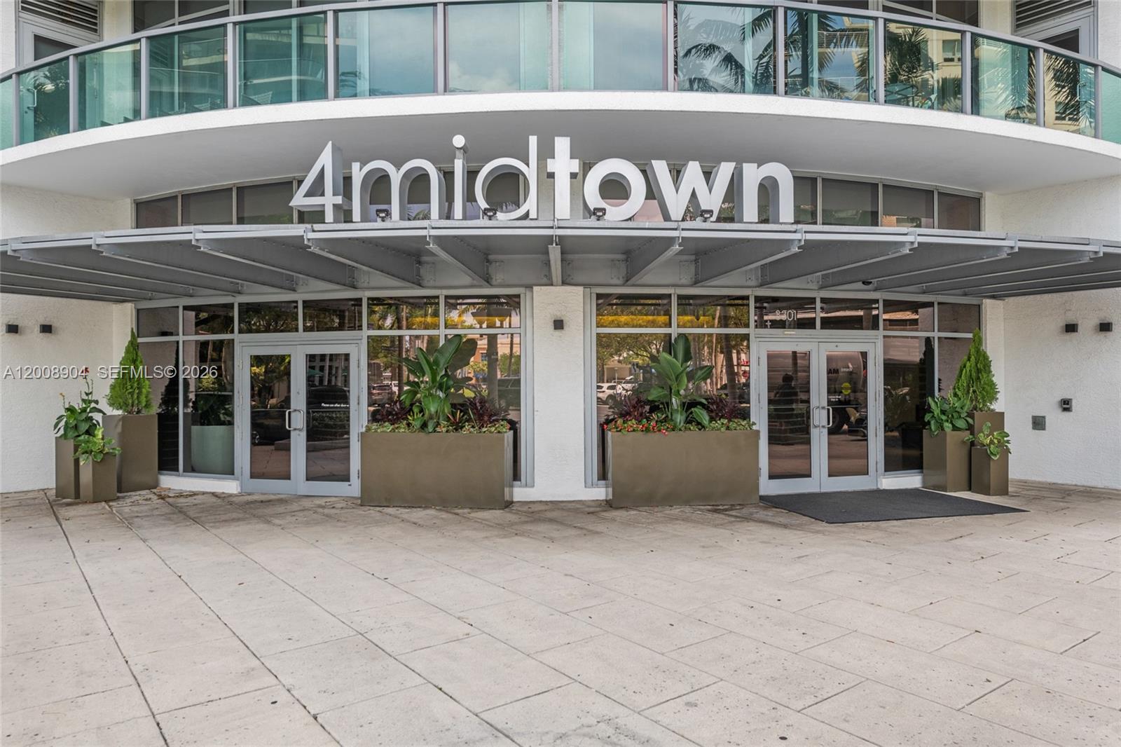 The exterior entrance of a modern building features glass doors, large planters, and signage — 3301 NE 1st Ave # H2011, Miami FL 33137, MIAMI, FL