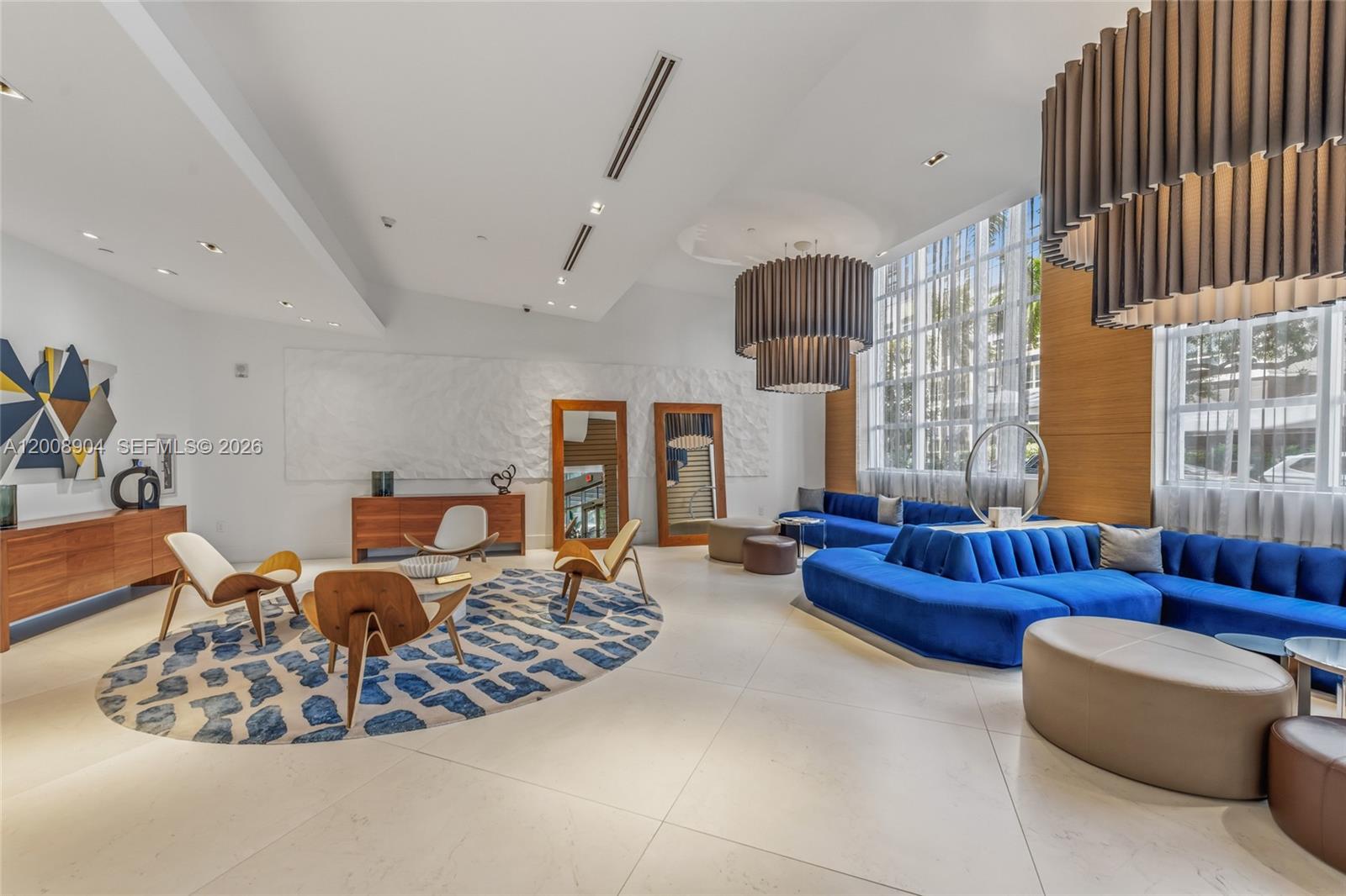A spacious, modern lounge features a large blue sectional sofa, wood-accented furniture, and circular rugs — 3301 NE 1st Ave # H2011, Miami FL 33137, MIAMI, FL
