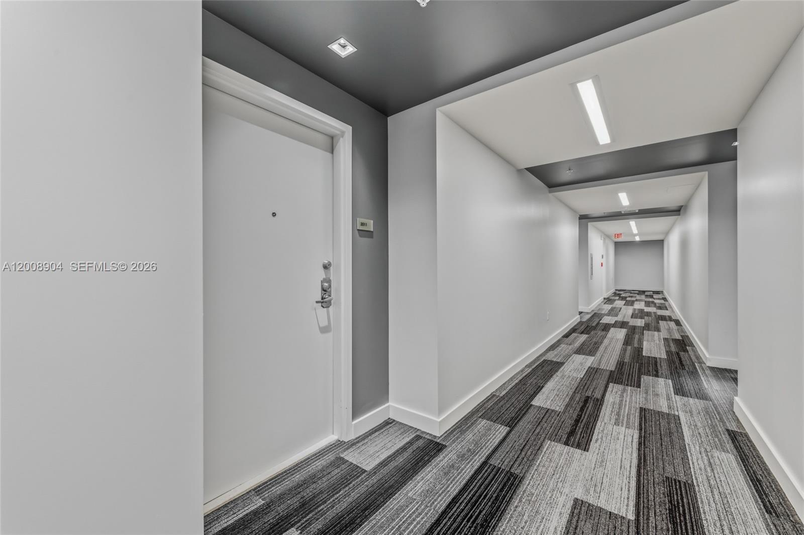 A modern apartment hallway features a white door, gray accent wall, and patterned carpet — 3301 NE 1st Ave # H2011, Miami FL 33137, MIAMI, FL