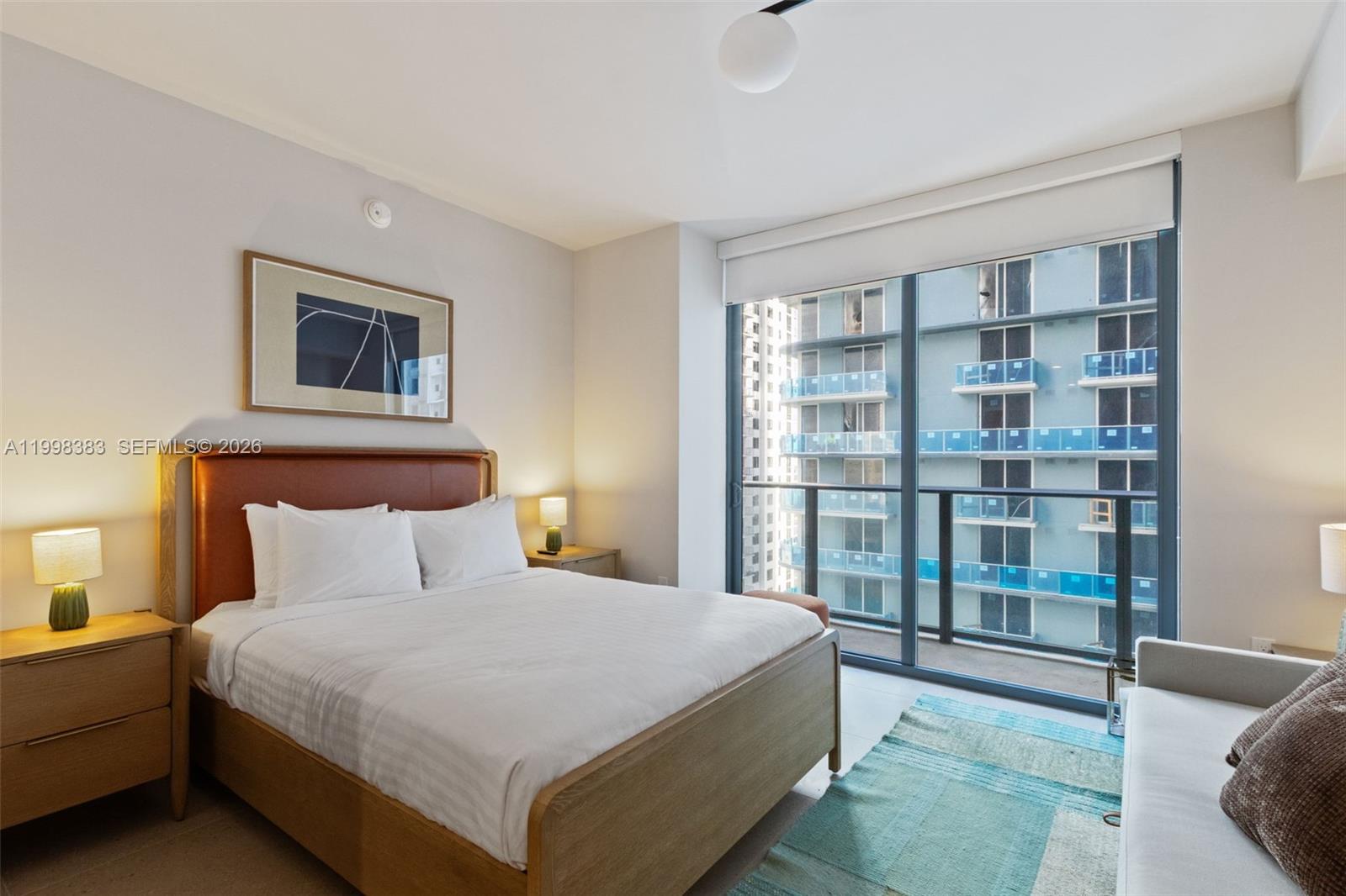 A bedroom features a wooden bed frame, two nightstands, and a large window overlooking buildings — 11 NE 6 # 2108, Miami FL 33132, MIAMI, FL
