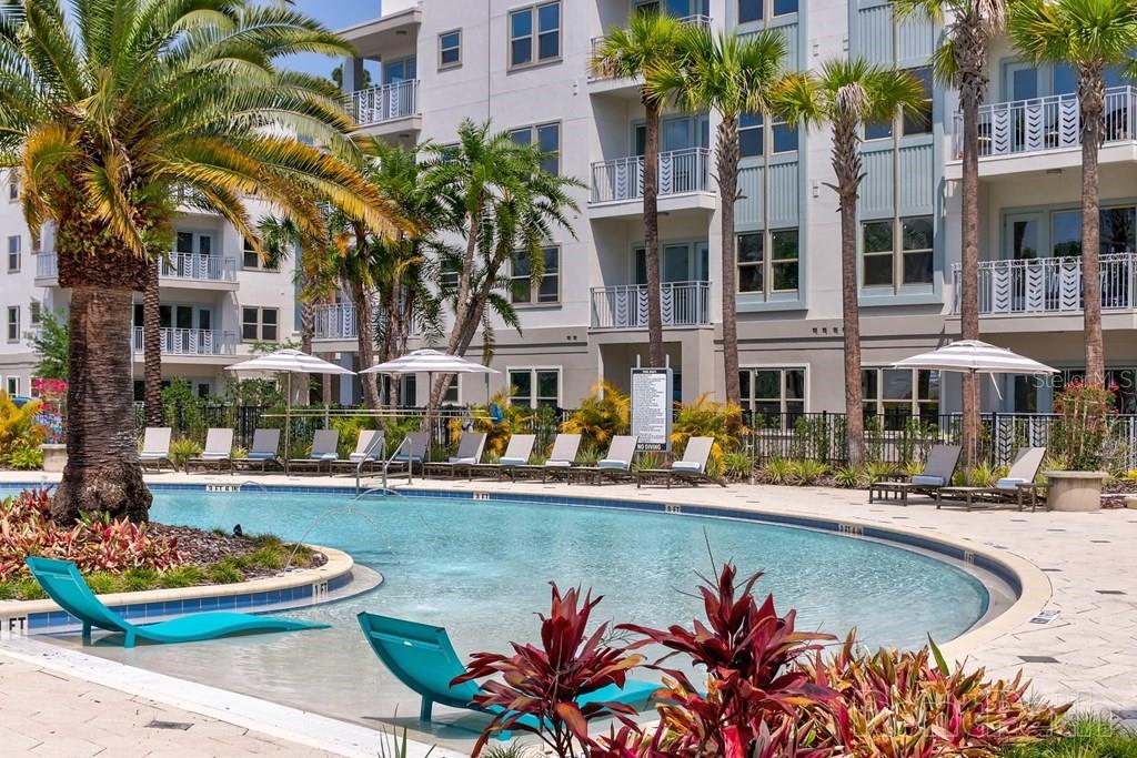 A swimming pool with lounge chairs sits in front of a multi-story apartment building — 1688 CELEBRATION BOULEVARD UNIT The Audrey, CELEBRATION, FL