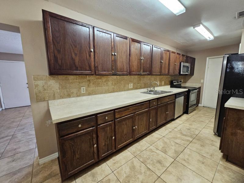 A kitchen features dark wood cabinets, light countertops, a tiled backsplash, and stainless steel appliances — 377 BRITTANY CIRCLE, CASSELBERRY, FL