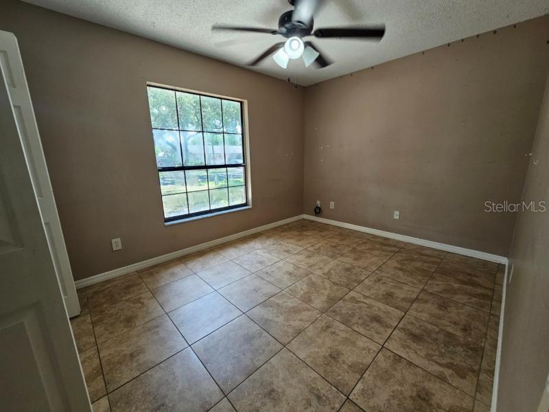 An empty bedroom features tan walls, a ceiling fan, and large square floor tiles — 377 BRITTANY CIRCLE, CASSELBERRY, FL