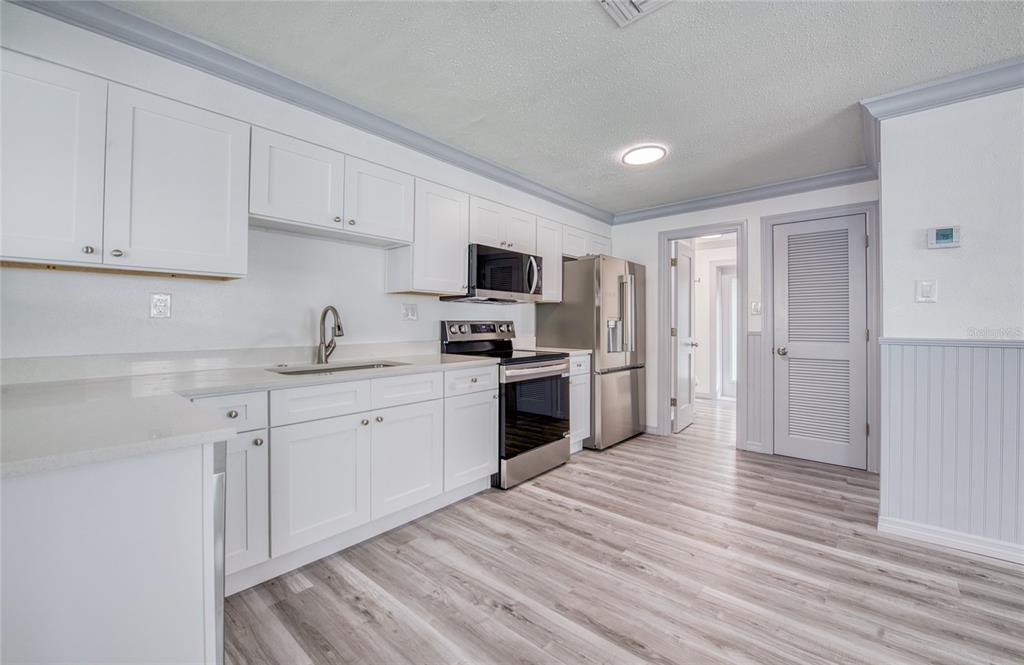 A kitchen features white cabinets, stainless steel appliances, and light wood-look flooring — 19506 GULF BOULEVARD UNIT 4, INDIAN SHORES, FL