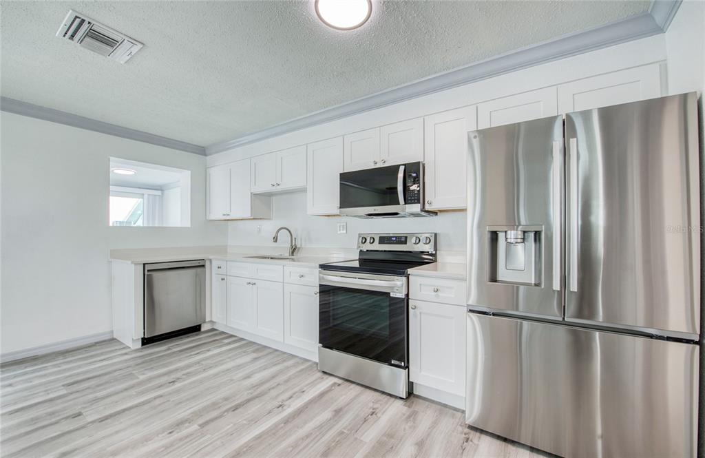 A kitchen features white cabinets, stainless steel appliances, and light wood-look flooring — 19506 GULF BOULEVARD UNIT 4, INDIAN SHORES, FL