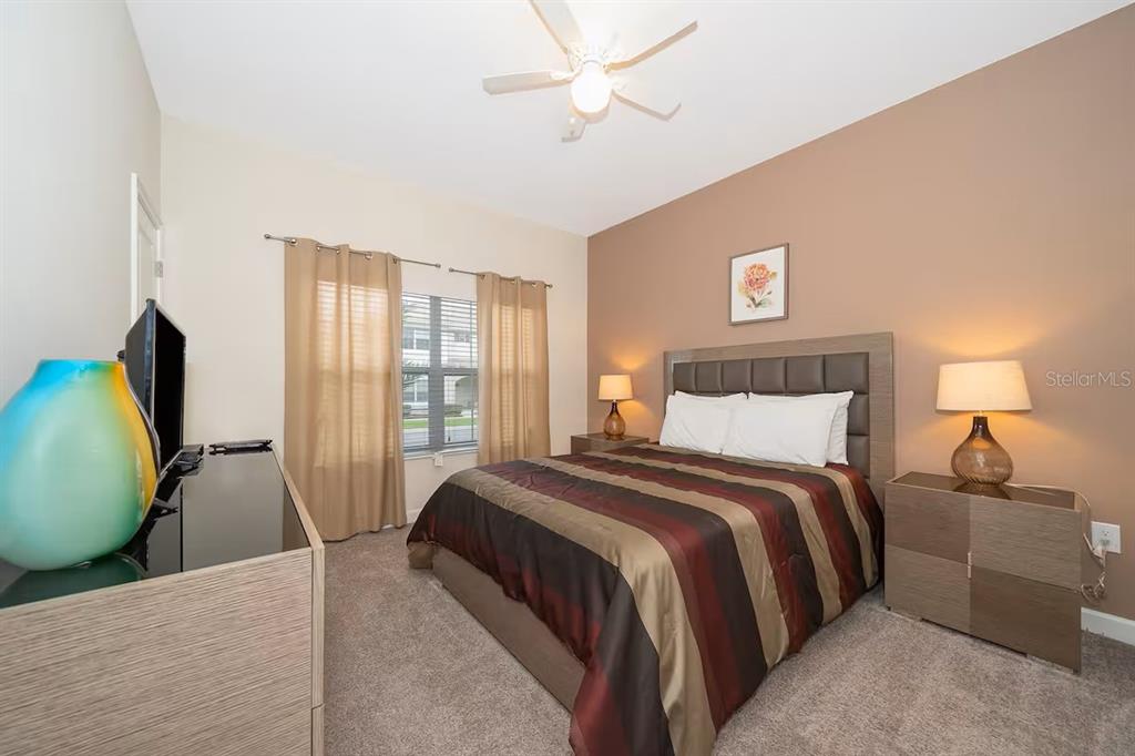 A bedroom features a bed with a striped comforter, two nightstands, and a ceiling fan — 4905 WINDERMERE AVENUE, KISSIMMEE, FL