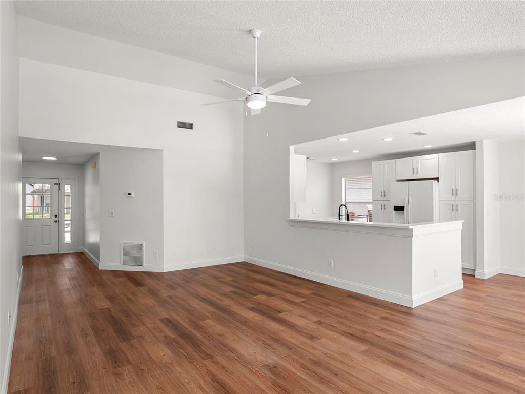 A living room with wood-look flooring, a vaulted ceiling, a ceiling fan, and an open kitchen — 605 WHITTINGHAM PLACE, LAKE MARY, FL