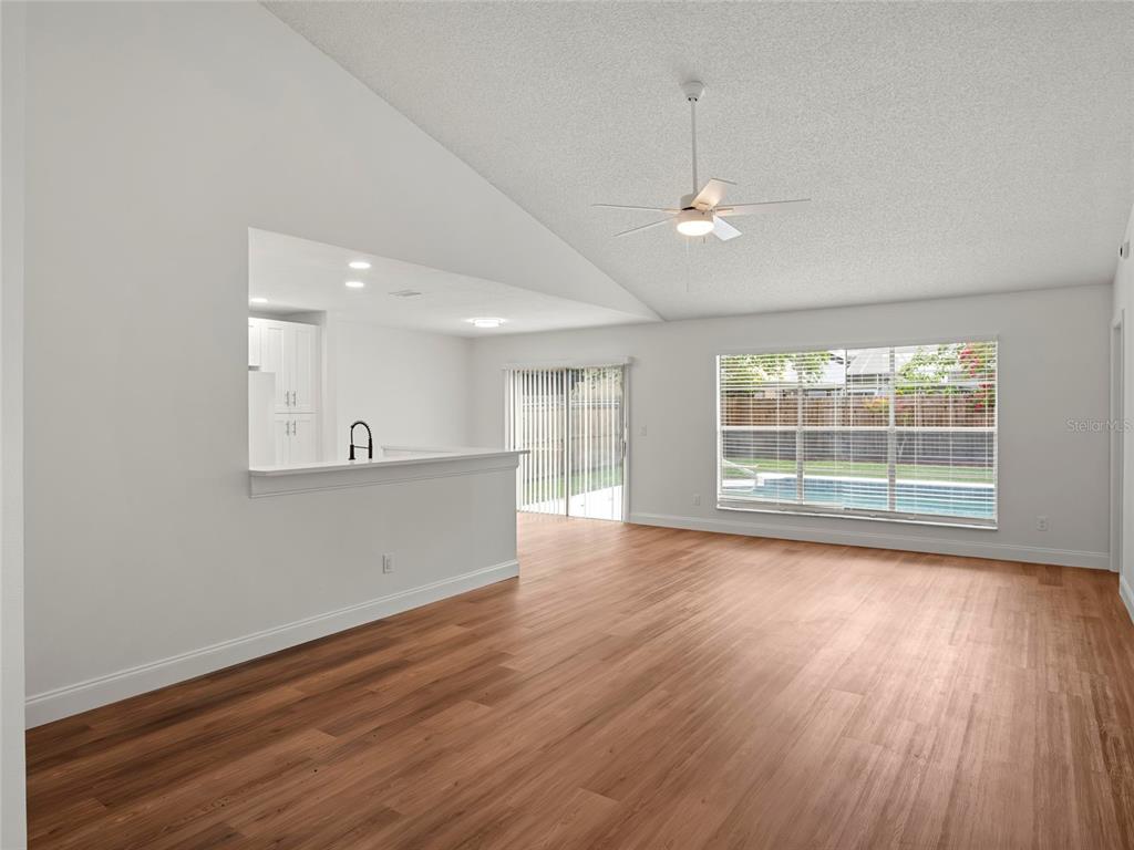 A bright living room with wood-look flooring, a ceiling fan, and a view of a pool — 605 WHITTINGHAM PLACE, LAKE MARY, FL