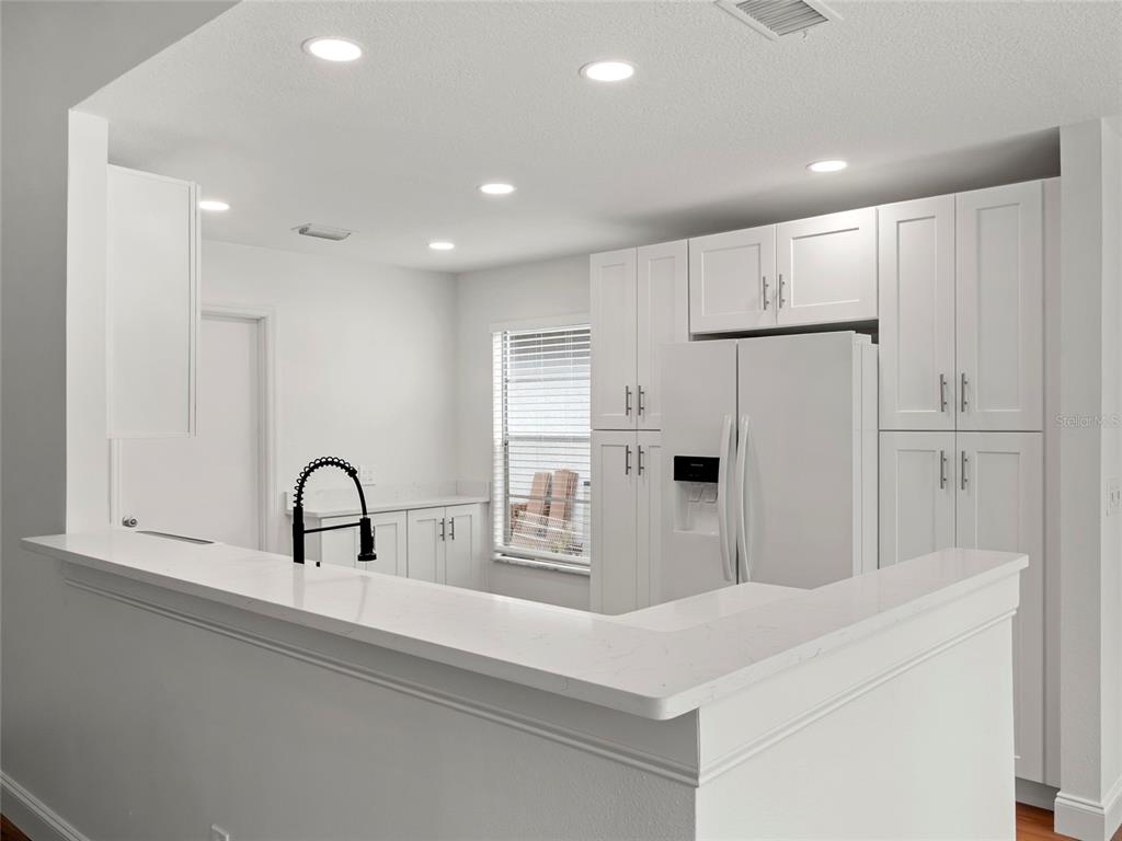 A white kitchen features quartz countertops, shaker-style cabinets, and a breakfast bar — 605 WHITTINGHAM PLACE, LAKE MARY, FL