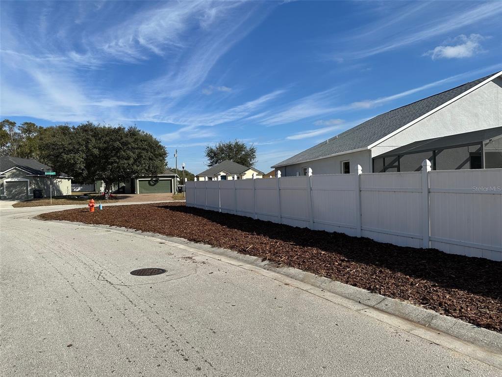 A white vinyl fence borders a mulched yard next to a paved residential street — 1354 KNOLLWOOD DRIVE, DAVENPORT, FL