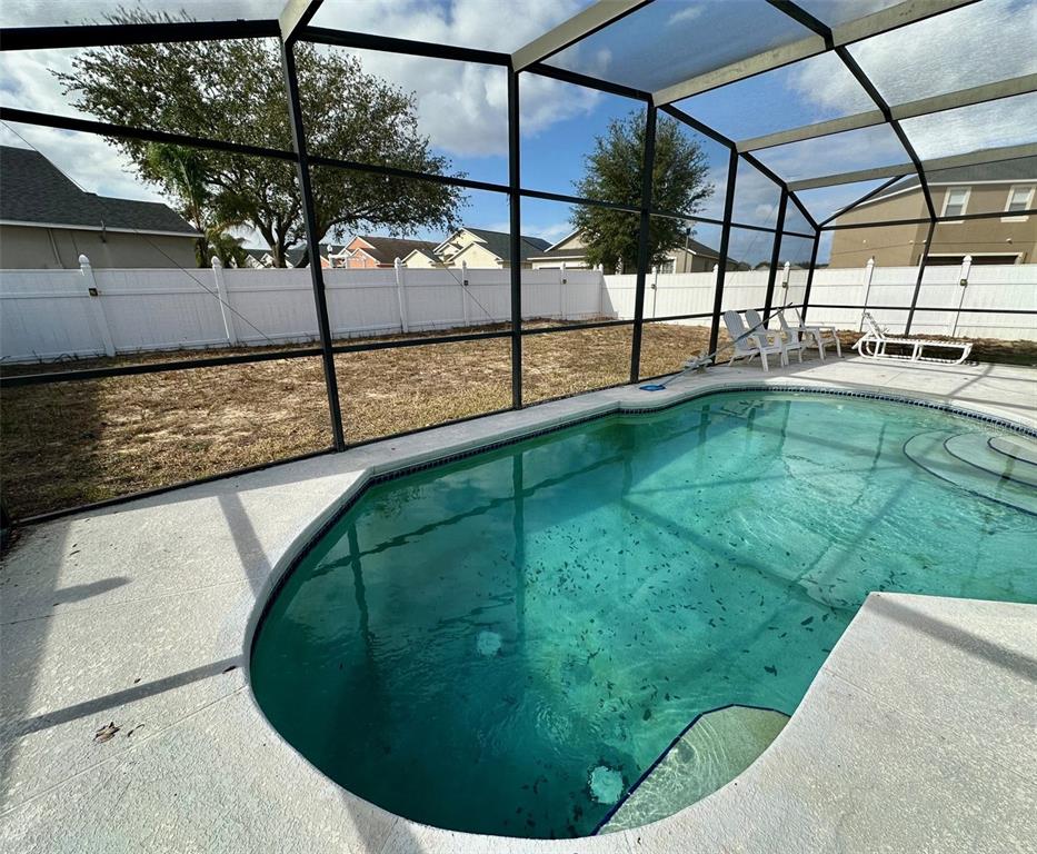 A screened-in swimming pool sits in a backyard enclosed by a white vinyl fence — 1354 KNOLLWOOD DRIVE, DAVENPORT, FL